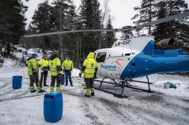 Mannskapet i varselklær ved helikopteret på snødekt bakke.