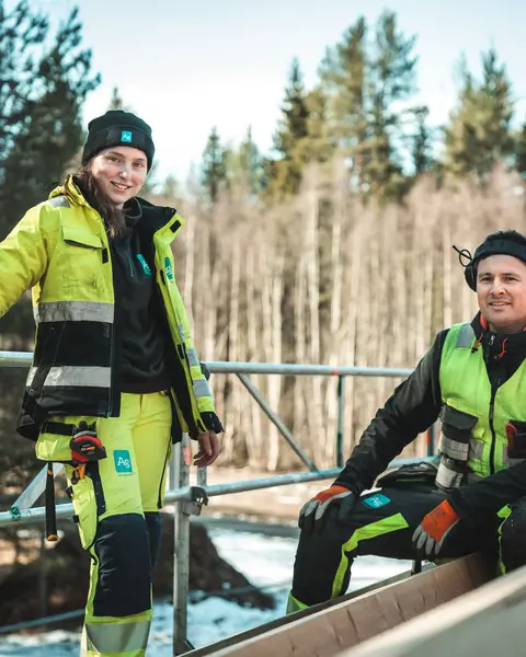 To fagarbeidere fra Ag i varselklær på en byggeplass i skogen.