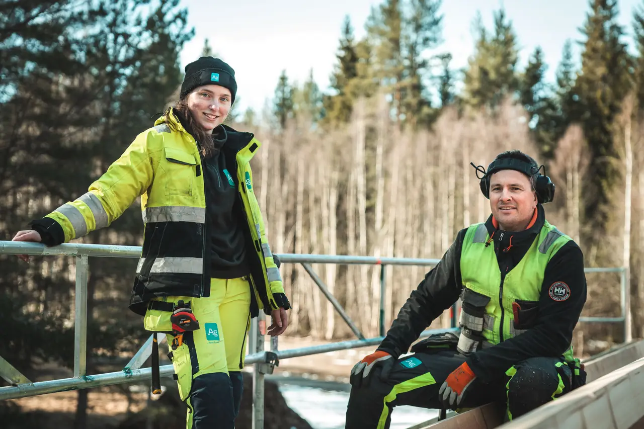 To fagarbeidere fra Ag i varselklær på en byggeplass i skogen.